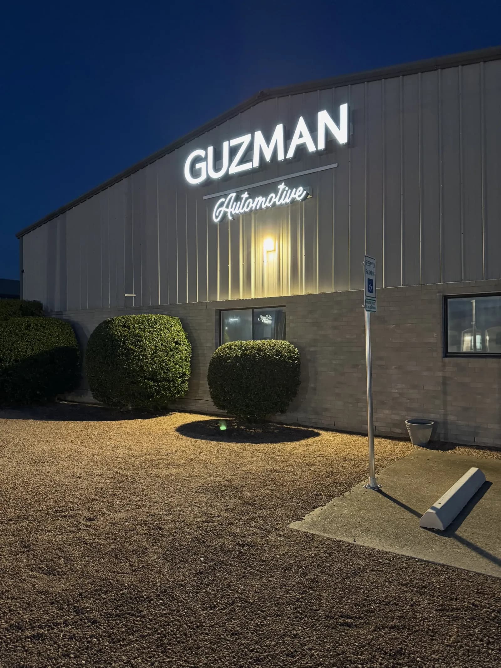 The illuminated Guzman Automotive sign on the Hutto, TX shop at dusk